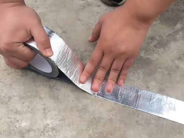 Aluminum foil butyl tape is used to seal a crack in the ground.